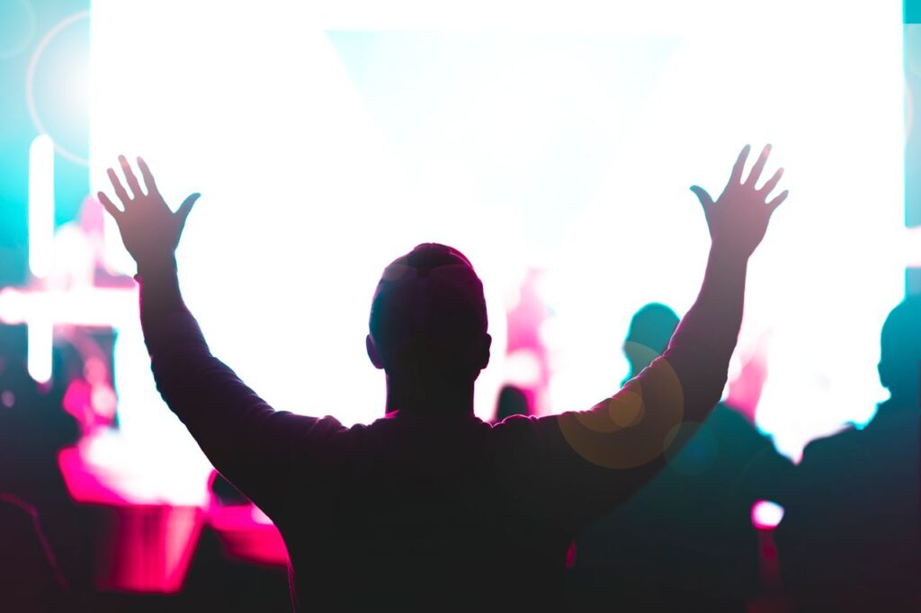 A person raises hands at a lively concert with vivid lights.